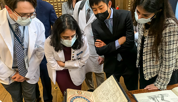 Four masked researchers lean over a manuscript from the historical library