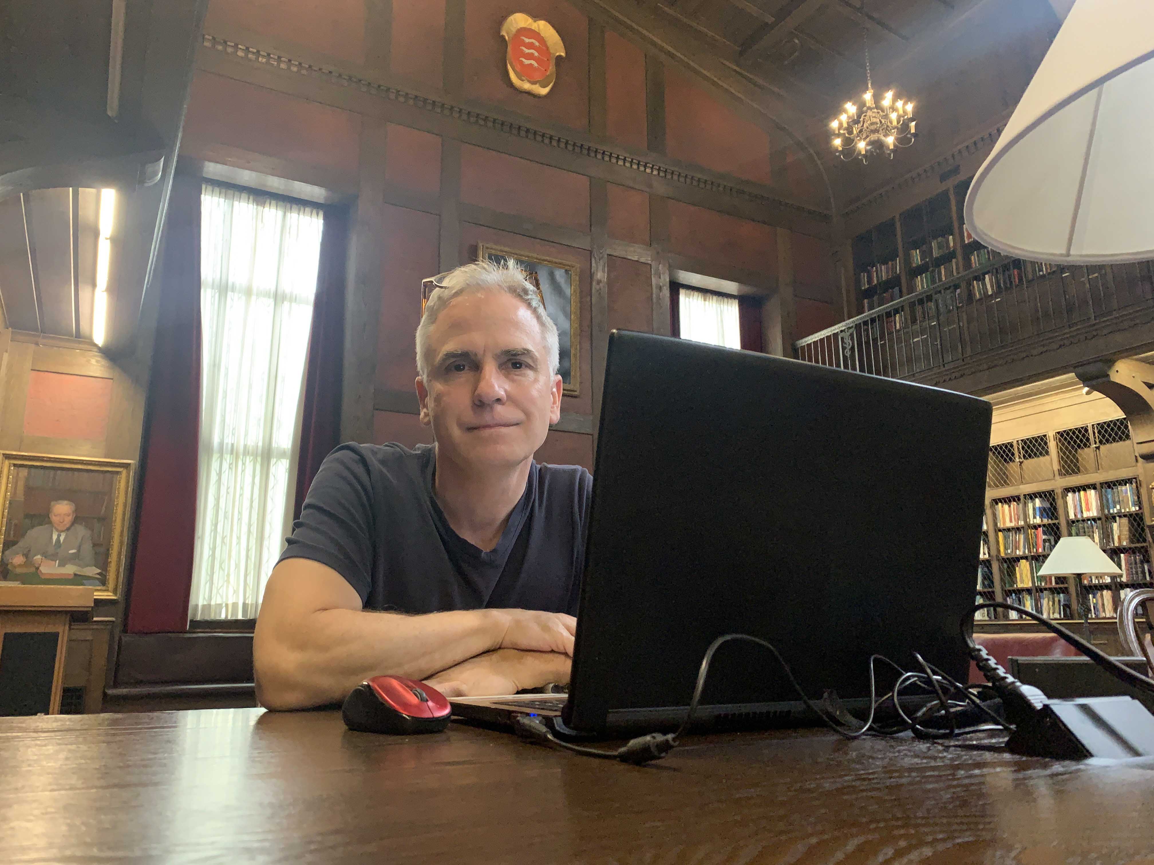 a man seated at a wood table in a wood-paneled library