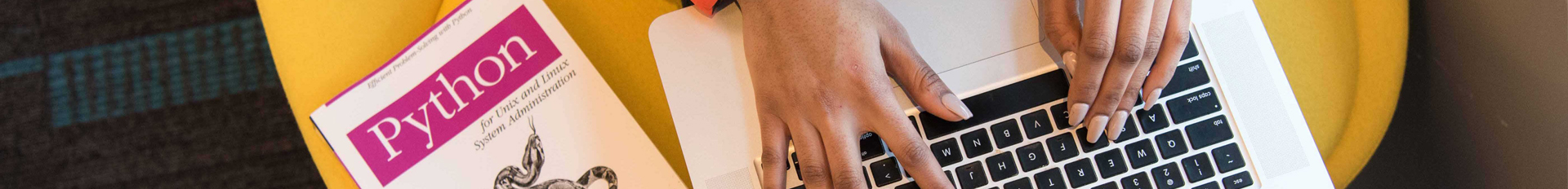 aerial view of black hands typing on a macbook with a book titled python nearby