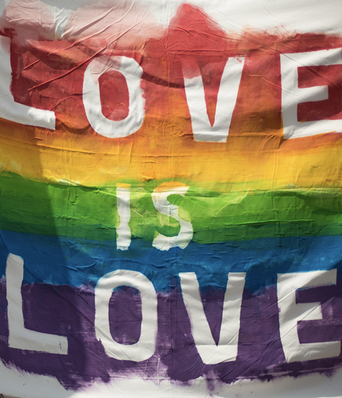 a sheet covered in horizontal rainbow stripes with the words Love is Love in white