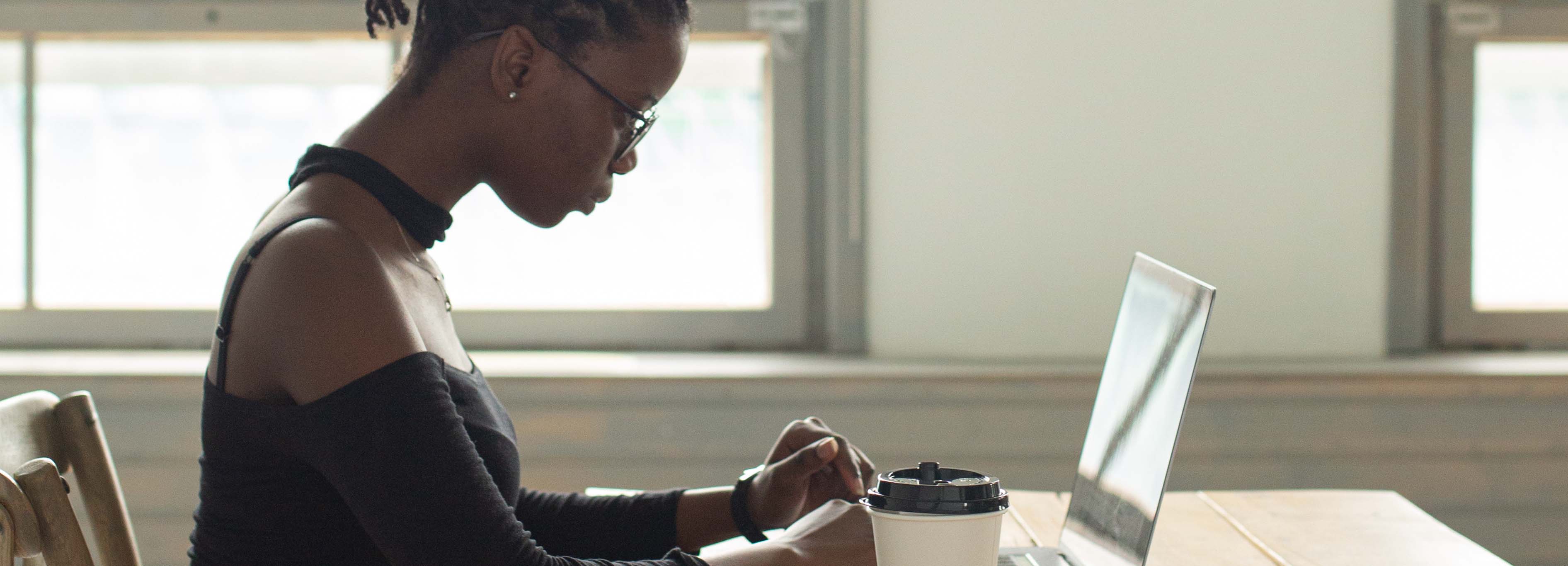 side view of a female-presenting black person typing on a laptop at a desk