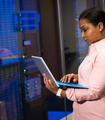 a woman types on an open laptop in front of a server room