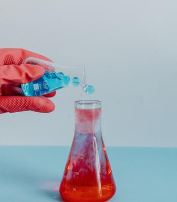 a gloved hand pours liquid from one beaker to the other